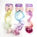 Long curly synthetic hair extension attached to clip; Pastel gradient colours including yellow, blue, purple and pink variations; Large pink glitter bow with multicoloured sparkles; Mounted on purple and cream branded backing card;