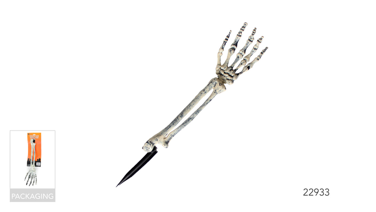 Off-white skeletal hand and long arm with dark distressed markings; Black pointed stake attached to the base; Product shown on orange retail packaging labelled “Skeleton Hand Garden Stake”;