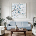 Square canvas print; Blue floral design with brown branches; White background; Wooden frame with depth; Displayed above sofa in room;