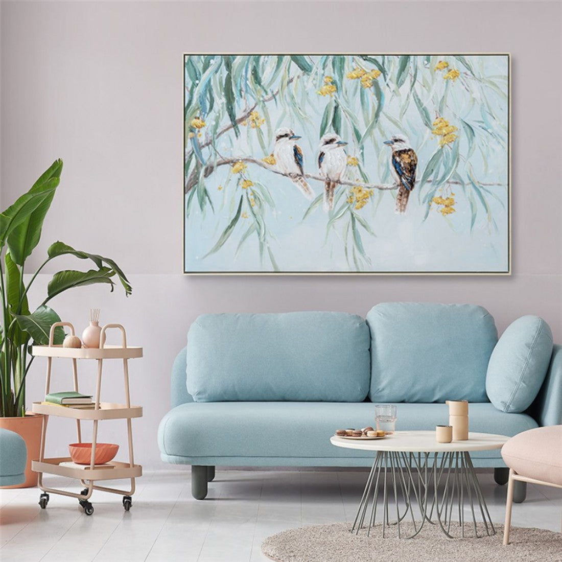 Hand painted canvas; Features three kookaburras on a branch; Light blue and green background; Yellow flowers accents; Framed canvas with slim border;