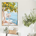 Canvas print with vibrant lemon tree and coastal view; Slim gold frame around the canvas; Soft pastel colour tones including blue, yellow and white; Dimensions approx 82.5x122.5x4.5cm; Hung on a neutral wall above a white couch;