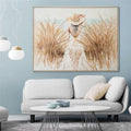 framed artwork; muted natural colours; woman wearing hat walking through tall grass; rectangular shape; approximate size 122.5x92.5cm;