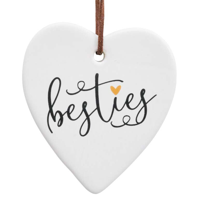 heart-shaped ceramic ornament; white creamy background; black script text 'besties'; small gold heart detail; brown faux-leather hanger strap;