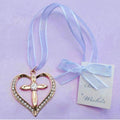 gold-tone heart shape with cross; ring of clear crystals in heart outline; pale sheer ribbon attached; small tag with blue bow;