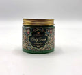 green body scrub visible through clear jar; decorative label with floral pattern; gold metal screw lid; jar holds 280g product;