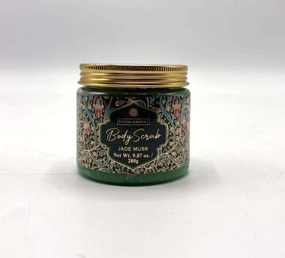 green body scrub visible through clear jar; decorative label with floral pattern; gold metal screw lid; jar holds 280g product;