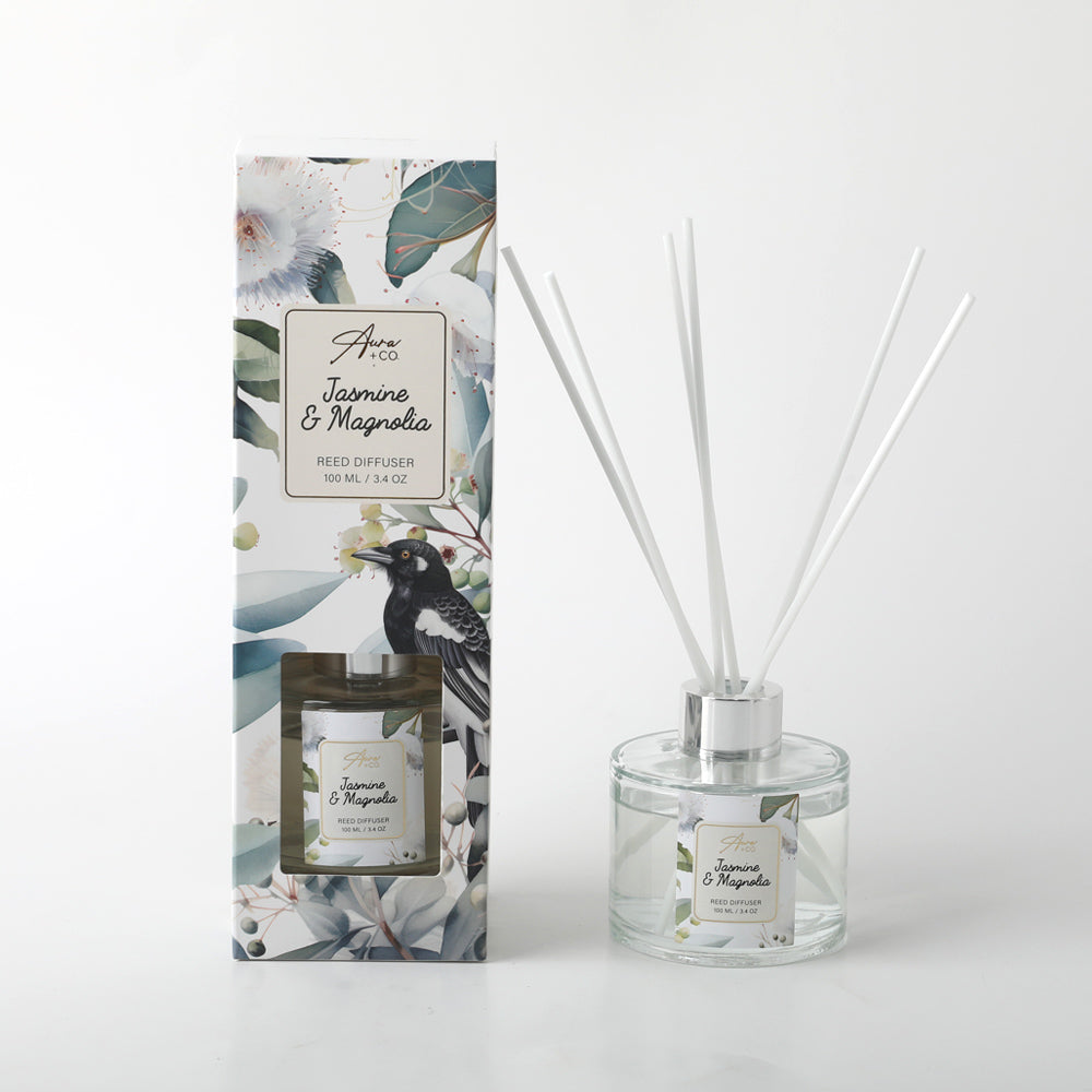 Clear glass round bottle with silver collar; White reed sticks; Floral and bird printed label on bottle and packaging; Tall rectangular packaging with botanical design;