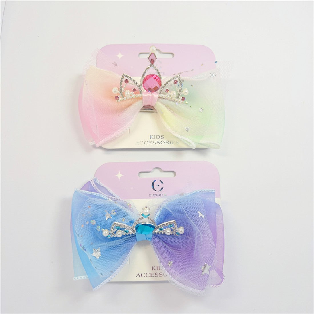 Large layered organza bow in gradient pastel colours; Metallic crown decoration with rhinestones and faux pearls; Glitter accents scattered across bow fabric; Mounted on branded backing card labelled “Kids Accessories”;