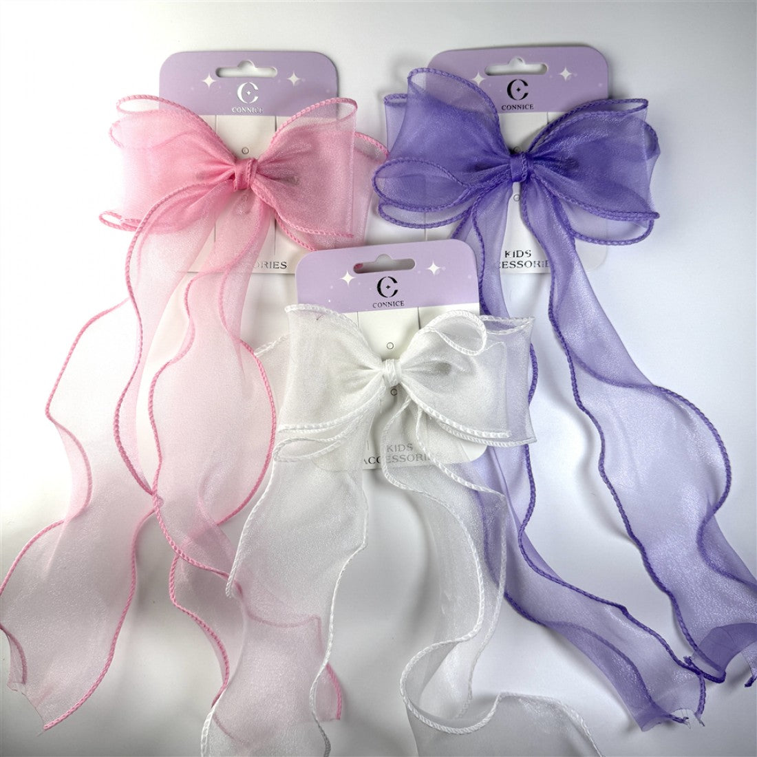 Large sheer organza bows with long wavy tails; Visible colours include pink, white and purple; Fabric has a soft shimmer finish; Edges of the ribbons are neatly stitched in matching colours; Each bow is carded on lilac branded packaging;