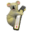 koala figure holding a tree trunk; attached thermometer with Celsius and Fahrenheit scales; resin material with textured fur details; natural grey and pink colouring on koala; vertical rectangular thermometer embedded in tree trunk;