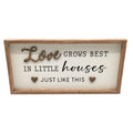 Rectangular wooden plaque with light timber frame; White background with black and wood-tone text; Raised wooden word "Love" and two small heart shapes; Quote reads "Love grows best in little houses just like this";