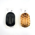 Oval-shaped hair clip with open centre; Matte black clip shown on display card; Tortoiseshell-style clip shown as alternate colour; Snap-style prongs visible inside the oval frame;