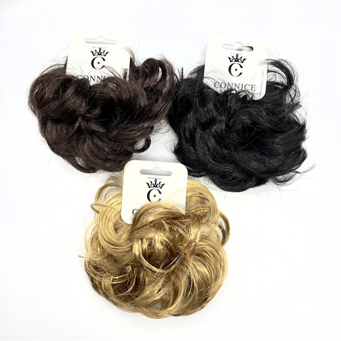 Curly synthetic hair styled as a bun; Shown in black, dark brown and blonde colours; Each piece attached to white branded hanging card; Compact, rounded bun shape suitable for updos;