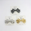 Double bow-shaped metal hair clip; Textured ribbed finish on bow; Spring-style metal clip backing; Shown in metallic silver, dark grey and gold tones; Mounted on white branded hair accessory card;
