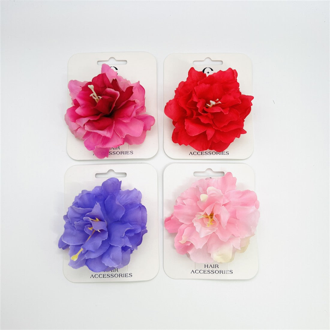 Large layered artificial flower shape; Available in pink, red, purple and light pink tones; Mounted on white backing card labelled “Hair Accessories”; Soft fabric-style petals with stamen detail in centre;