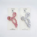 Two bow-shaped claw clips displayed on backing cards; One clip is translucent pink and one is translucent white; Both clips feature small silver bead studs; Gold-toned metal claw mechanism is visible; Packaging is branded "Connice" with "Hair Accessories" text;
