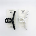 Long cross-shaped claw clip design; One black clip and one white clip shown; Silver bead studs along the arms of the clip; Mounted on branded backing cards labelled "Connice"; Curved teeth visible on inner edge of clip;