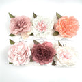 Large layered fabric flower design; Soft pastel colours including pink, white and peach; Green fabric leaf accents behind the bloom; Mounted on branded white display cards;