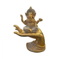 Gold-tone resin figurine of Ganesh; Ganesh seated cross-legged on an open hand; Ornate patterned base supporting the hand; Detailed headdress and jewellery on figurine;