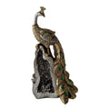 Gold-toned peacock figurine with intricate embossed detailing; Green jewel-like accents on tail feathers; Peacock perched on a grey geode-style rock base; Overall vertical ornament measuring roughly 29cm tall;