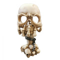Beige bone-style skull with darker shading in crevices; Candle holder formed by elongated skull and jaw details; Base made of multiple small skulls; Dark metallic-look chain wrapped around the stem; Matte resin-like finish;