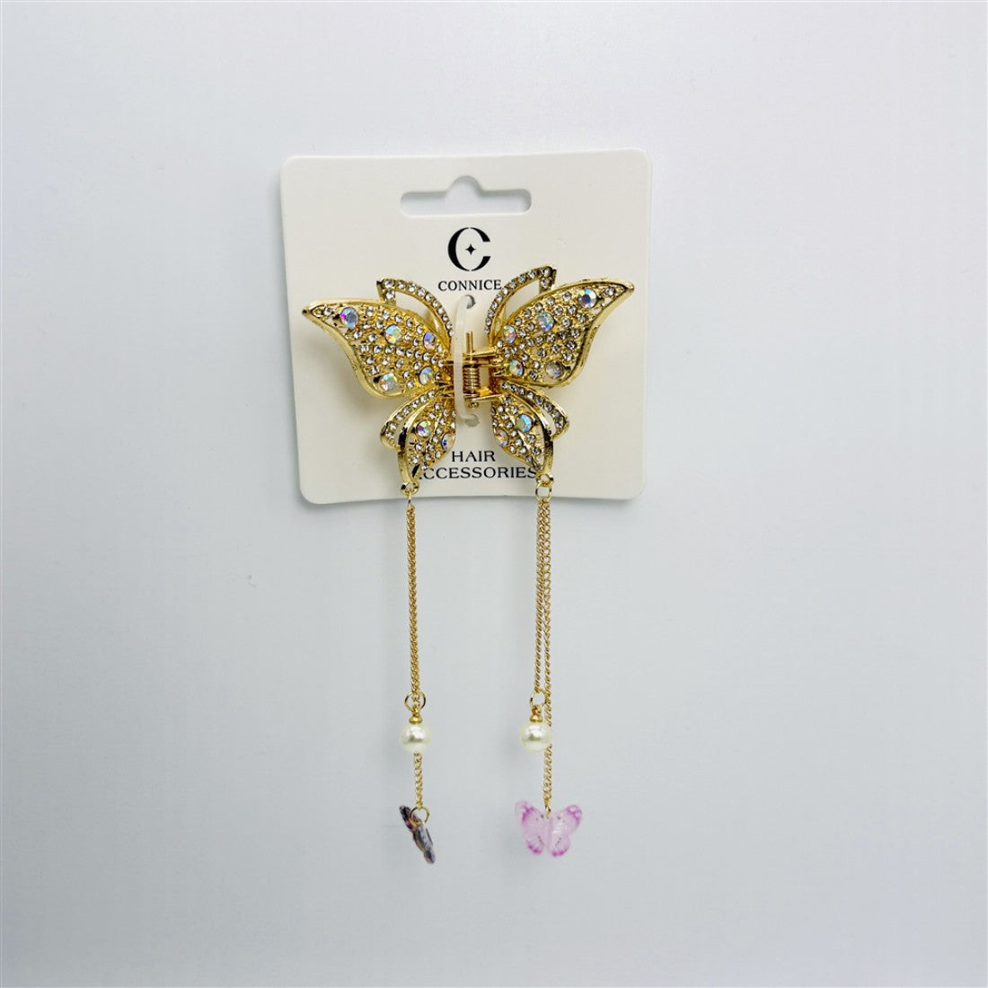 Gold-tone metal butterfly-shaped claw clip; Covered in clear rhinestones; Two gold chains hanging from the bottom of the clip; Chains finished with faux pearls and small butterfly charms; Packaged on a white backing card labelled hair accessories;