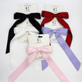 Large satin bow with long ribbon tails; Shown in black, white, red, lilac and pink colours; Mounted on branded backing card labelled hair accessory; Soft, smooth fabric with a slight sheen;