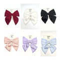 Large satin fabric bow with long tails; Shown in multiple solid colours including red, white, black, pink, lilac and light blue; Mounted on branded backing card labelled as hair accessory; Soft, slightly shiny fabric texture;
