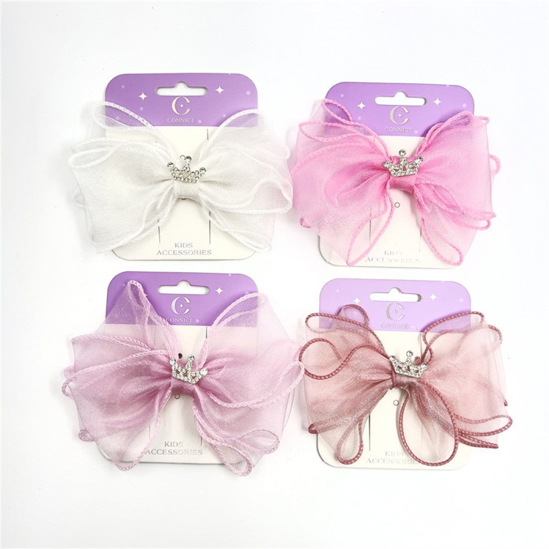 Large sheer organza bows in soft pink and white tones; Silver crown charm with small rhinestone-style details at the centre; Mounted on purple and cream backing cards labelled kids accessories; Wide, layered bow shape with gently curled edges;