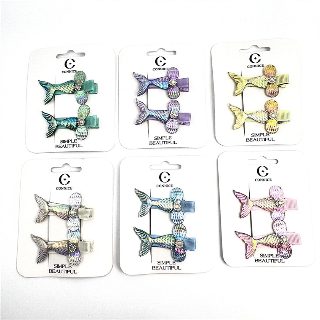 Mermaid tail-shaped hair clips with textured scale pattern; Glittery, iridescent finish on the tails and bows; Each card shows two matching clips on backing card; Various pastel colour combinations displayed on packaging;