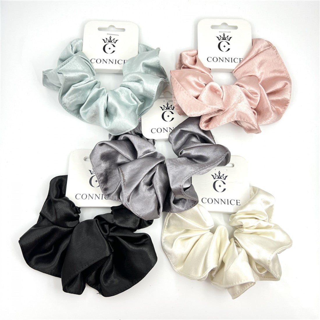 Shiny satin fabric with smooth texture; Scrunchies shown in solid colours including black, cream, pink, grey and light green; Chunky, gathered design for a full look; Each scrunchie displayed on branded CONNICE card packaging;
