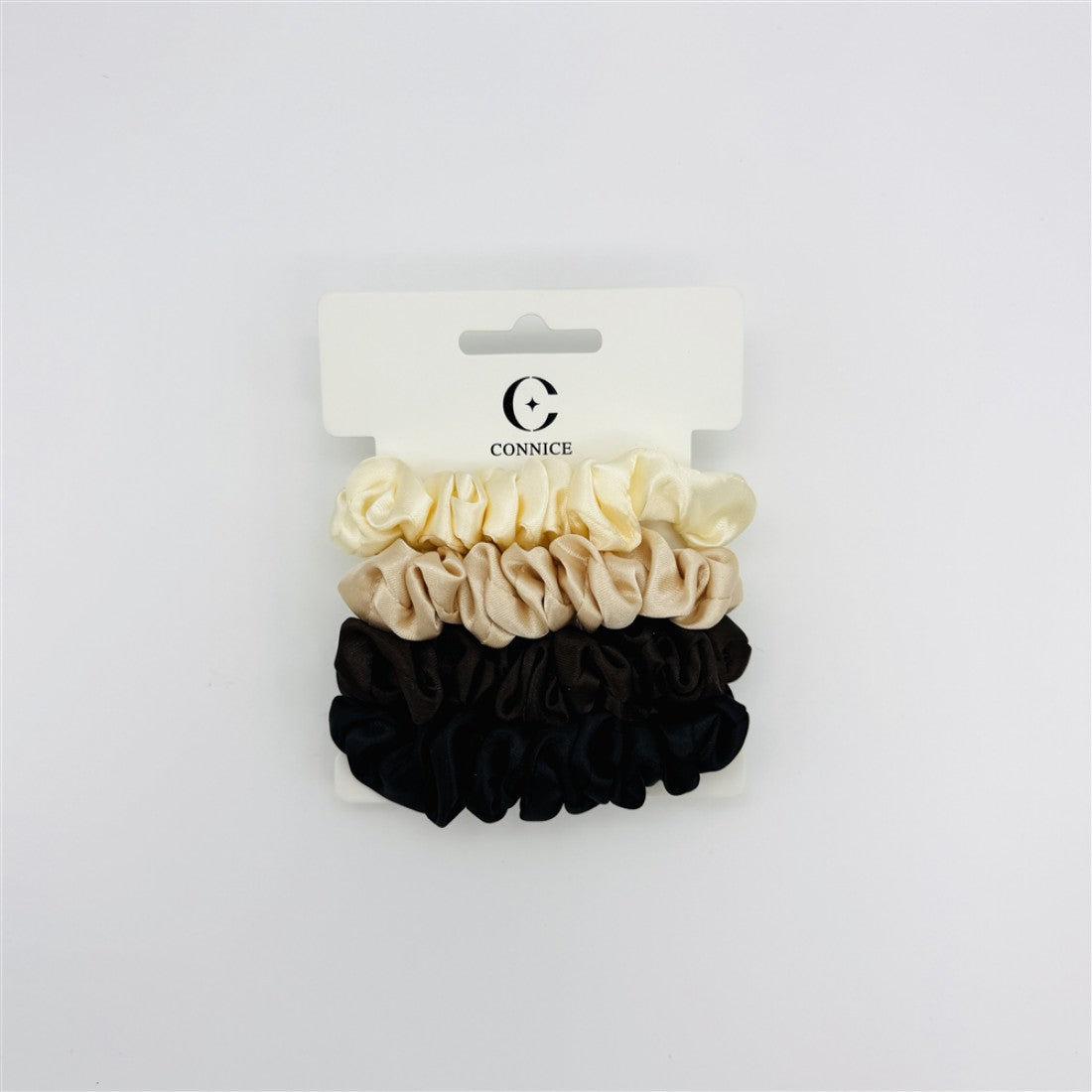 Four small scrunchies in cream, beige, dark brown and black tones; Smooth satin-look fabric with gathered design; Scrunchies arranged vertically on a white display card; Brand name and logo printed on the top of the card;