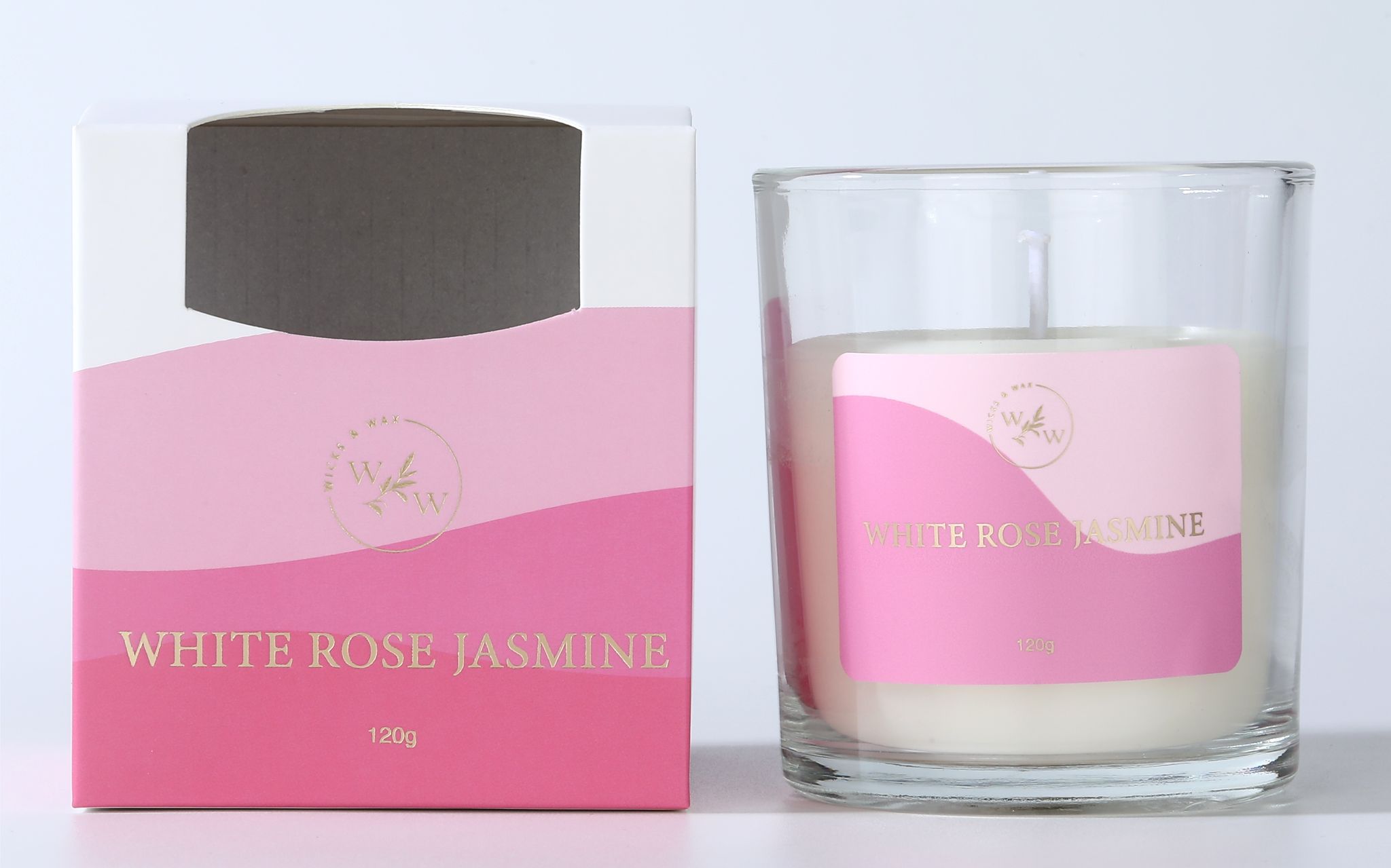 Candle in clear glass container; White wax candle; Pink label with gold text; Matching pink and white cardboard box packaging;