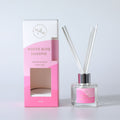Clear glass round bottle; Silver coloured metal collar; Five white reed sticks; Pink packaging box with cutout window; Pink label with gold text;