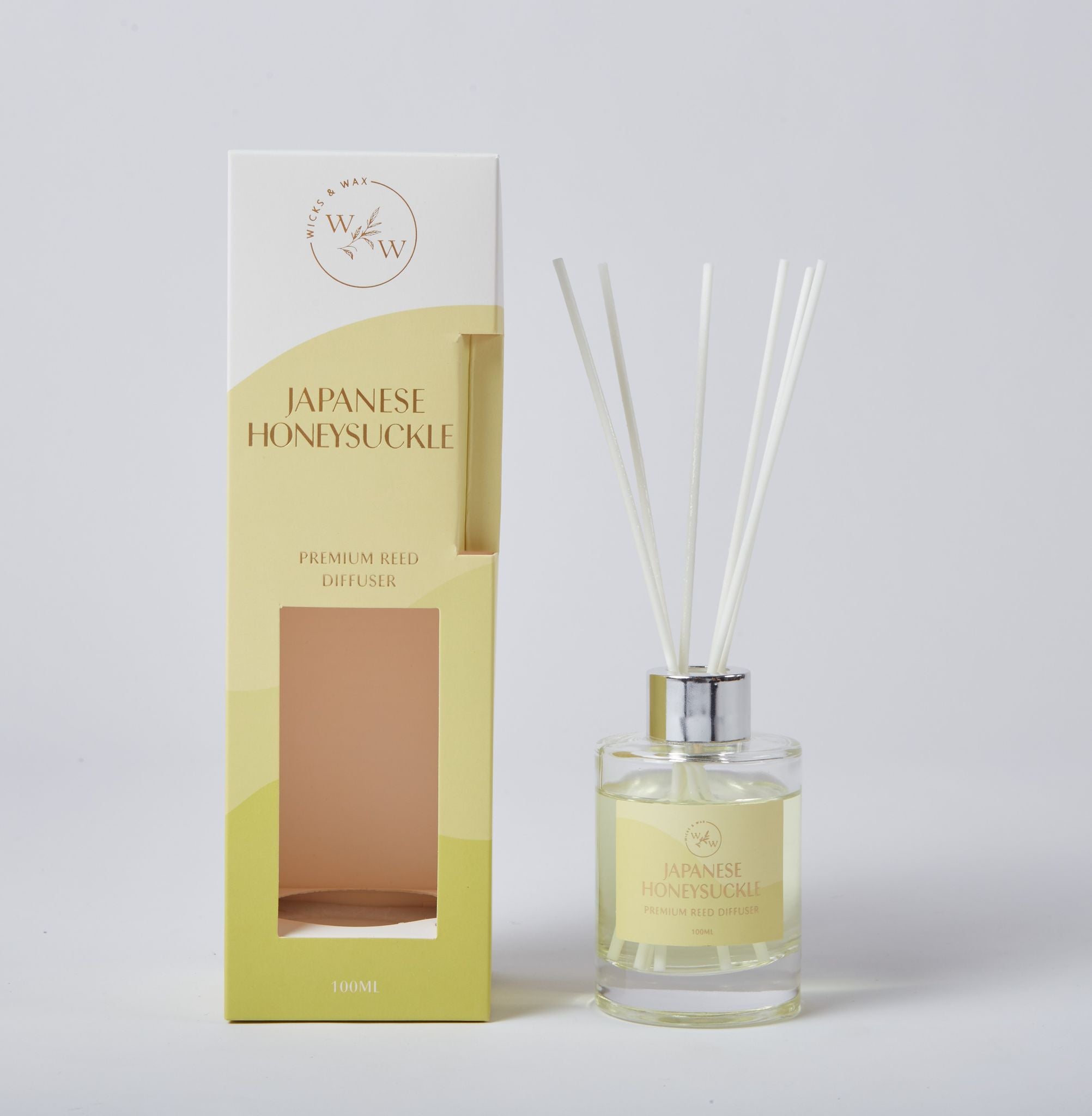 Clear glass bottle with silver collar; Yellow label with text 'Japanese Honeysuckle'; Multiple white reed sticks; Soft yellow and white packaging box; 100ml volume indicated;