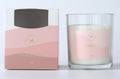 Clear glass container; Pink and white label with gold lettering; Box packaging with matching pink tones; White wax inside glass;
