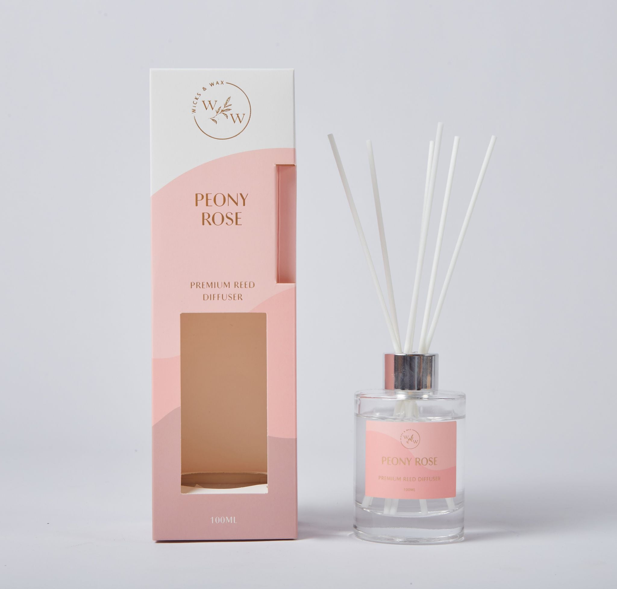 clear glass bottle with silver collar; pink label on bottle; white reed sticks; pink and white packaging box with window;
