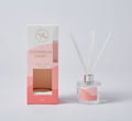 Pink and white box with gold text; Glass bottle with pink label; Includes white reed sticks; Silver collar on bottle;