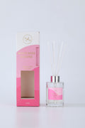 clear glass bottle; silver-coloured cap; white reed sticks; pink and white packaging box; gold foil text on packaging;