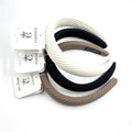 Wide padded headband shape; Ribbed textured fabric covering; Neutral colours including black, white and beige; Branded hang tags attached to each headband;
