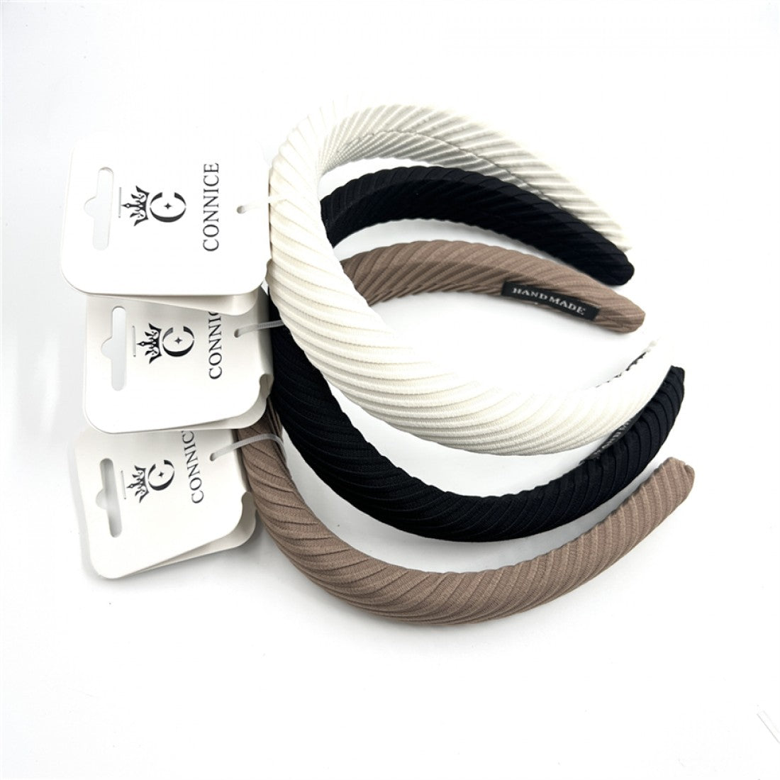 Wide padded headband shape; Ribbed textured fabric covering; Neutral colours including black, white and beige; Branded hang tags attached to each headband;