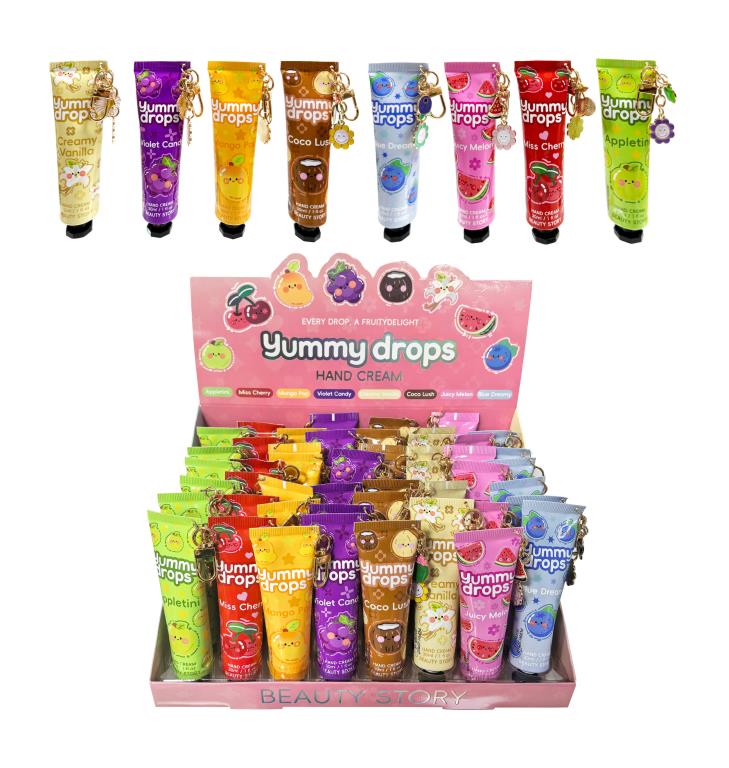 Colourful slim tubes with fruit-themed designs; Each tube has an attached keychain charm in various shapes; Multiple scent names visible on tubes (e.g., Creamy Vanilla, Violet Candy); Tubes arranged in pink display box labelled 'Beauty Story'; Bright, assorted colours including green, red, yellow, purple, brown, blue, and pink;